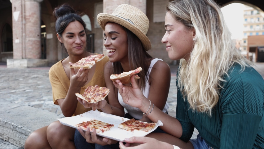 Three cheerful multiracial women eating pizza in the street - Happy millennial friends enjoying the weekend together while sightseeing in Italy - Young people lifestyle concept Royalty-Free Stock Footage #1088930353