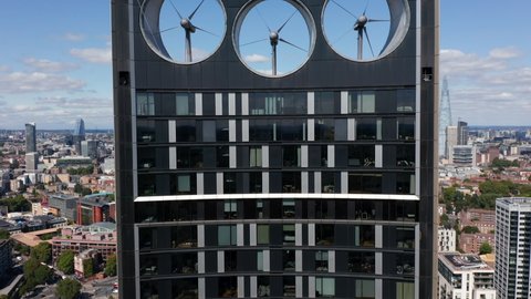 Ascending footage of top of Strata skyscraper with three big wind turbines for producing sustainable energy. Birds eye view of traffic of surrounding roads. London, UK
