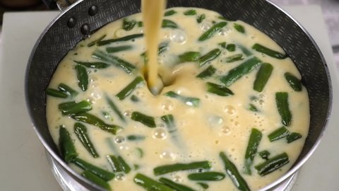 cooking an omelet with vegetables. cut and pan-fried green beans pour beaten eggs. the omelet stream gradually covers the whole beans. cook delicious and healthy food yourself. close-up. slow motion.