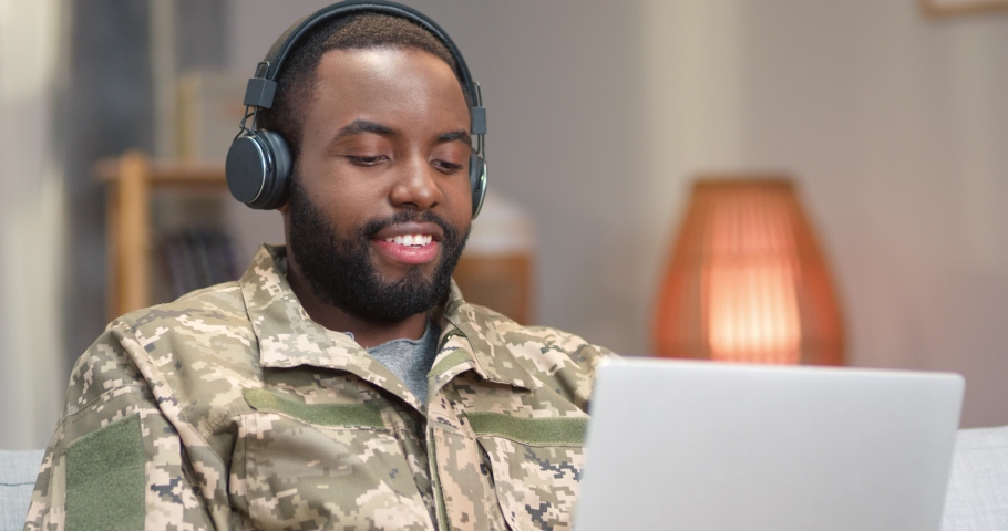 African military man in headphones using laptop on couch