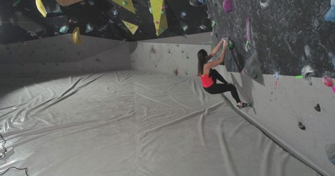 Bouldering, female climber training on a climbing wall, young woman practicing rock-climbing, mountaineer training.