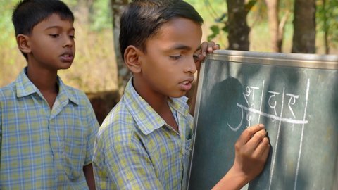 Indian Rural primary students wearing uniforms solving a mathematical problem on a board using chalk along with a male and female classmate in a village, Kudal, Maharashtra, India (March 2022)