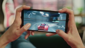 Female is Relaxing on a Couch at Home, Playing an Interactive Racing Drift Video Game on Her Smartphone. Gamer Lies on a Sofa in Living Room. Close Up POV Footage of Mobile Device Screen.