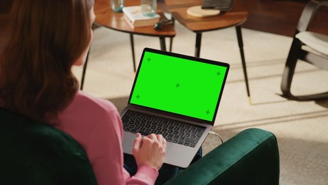 Young Adult Woman Working from Home Loft Apartment on Laptop Computer with Green Screen Mock Up Display. Creative Female Browsing the Web, Writing on Social Media. Close Up Over the Shoulder Footage.