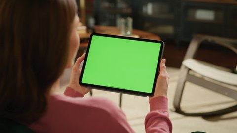 Female Holding Tablet Computer with Green Screen Mock Up Display. Woman Relaxing at Home, Watching Videos and Reading Social Media Posts on Mobile Device. Close Up Over the Shoulder Footage.