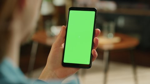 Man Swiping on Display and Scrolling Feed on Smartphone with Green Screen Mock Up Display. Male Resting at Home, Checking Social Media on Mobile Device. Close Up Over the Shoulder Footage.