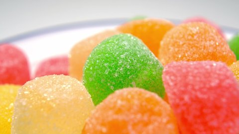 Multicolored marmalade candy with sugar in white plate. Gelatin sweet snack. Macro. Rotation