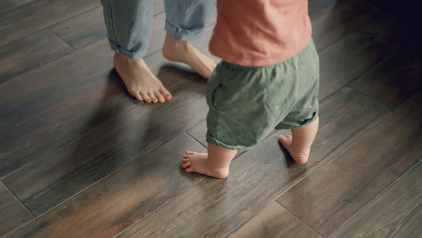 Little feet walking on floor, close-up. Baby learning to walk at home. Baby first steps. Smiling caring mother and cute little infant child girl cuddling in bedroom. Mum and child tender moments. Royalty-Free Stock Footage #1088939147