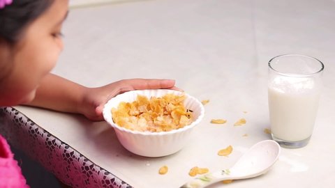 Slow motion video of an Indian girl child eating cornflakes and milk side facing