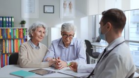 Happy senior couple having appointment with doctor in medical center. Therapist in mask tell good news to elderly man and woman in hospital office - Powered by Shutterstock - Get 15% off with code: PIKWIZARD15