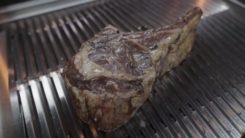 A large tomahawk steak is fried on a grill grid. A juicy piece of meat is being prepared. Fatty junk food. Close-up shot.