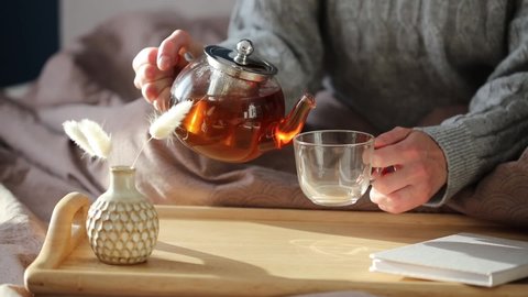 Woman pouring tea in mug from glass teapot. Cozy home hygge style interior. Tea ceremony at breakfast.