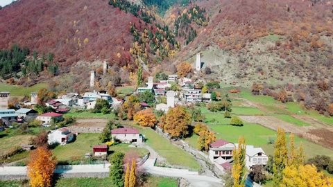 A bird's-eye view of a village or city on a hilly terrain. Mestia settlement in Svaneti in Georgia. The drone flies over the ancient Svan towers against the background of a yellow autumn forest.