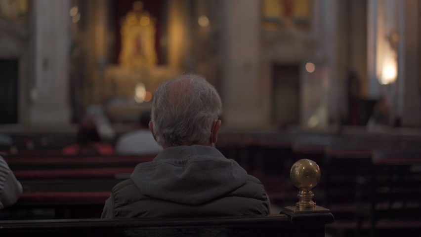Elderly man prays while sitting on bench inside church, rear view. Catholic Church inside evening prayer, dark mystic atmosphere Man sitting pew at Church and meditating, faith and religion concept | Shutterstock HD Video #1088947385