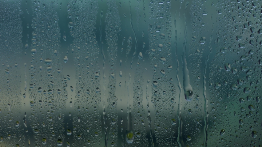 Water drops descend on the window in rainy weather against the blue sky in the forest, natural beautiful weather outside the city, transparent raindrops on the glass. Slow motion, 8K downscale, 4K.