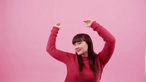 Full of energy positive caucasian brunette throwing hands in the air and smiling over pink background. Studio shot. High quality 4k footage