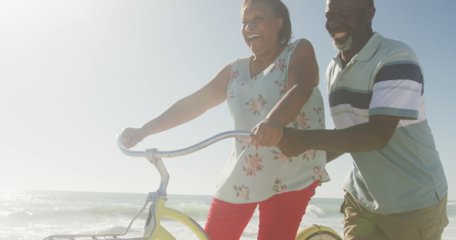 Smiling senior african american couple riding bicycles on sunny beach. healthy, active retirement beach holiday. Royalty-Free Stock Footage #1088950689