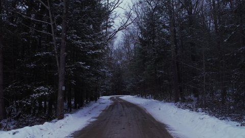 Smooth drone footage of a beautiful road through a snowy winter forest in the Appalachian mountains during winter in New York's Hudson Valley in the Catskill Mountains sub-range