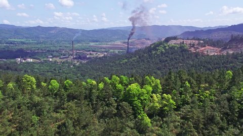 Aerial forward over verdant landscape with smoking chimneys in nickel mine, Loma Miranda. Falconbridge or Falcondo, Dominican Republic