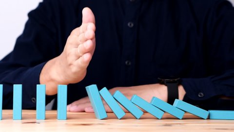Businessman hand fail stopping continuous falling domino wooden effect. Concept of Risk Management, Business Crisis, Domino Effect, Investment, Finance, Risk, Disaster, Protection, Prevention