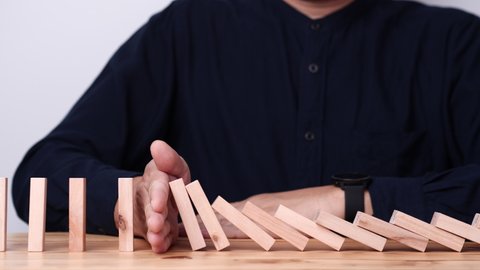 Businessman hand stopping continuous failing domino wooden effect. Concept of Risk Management, Business Crisis, Domino Effect, Investment, Finance, Risk, Disaster, Protection, Prevention, Opportunity
