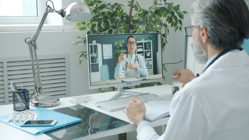 Man and woman doctors discussing pills holding bottles during online video call using pc in hospital. Medicine and communication concept. Royalty-Free Stock Footage #1088959089