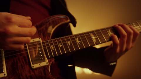 Professional guitarist hands playing electric guitar on show stage night club. Close up musician fingers running fretboard virtuously at spotlights. Unknown player performing music on party.