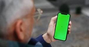 A man using mobile phone with green screen shaking his finger across the screen to the side, unrecognizable person, top view from behind the man's shoulder. Chroma key, mockup. Video in 4k, red komodo