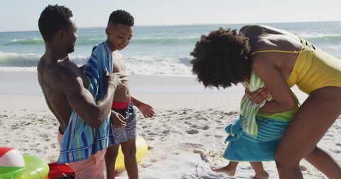 Smiling african american parents toweling off their children on sunny beach. healthy, active family beach holiday.