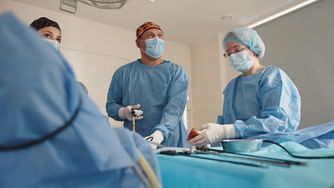 Process of gynecological surgery operation using laparoscopic equipment. Group of surgeons in operating room with surgery equipment. Waist up portrait of nurses in protective masks and sterile gloves.