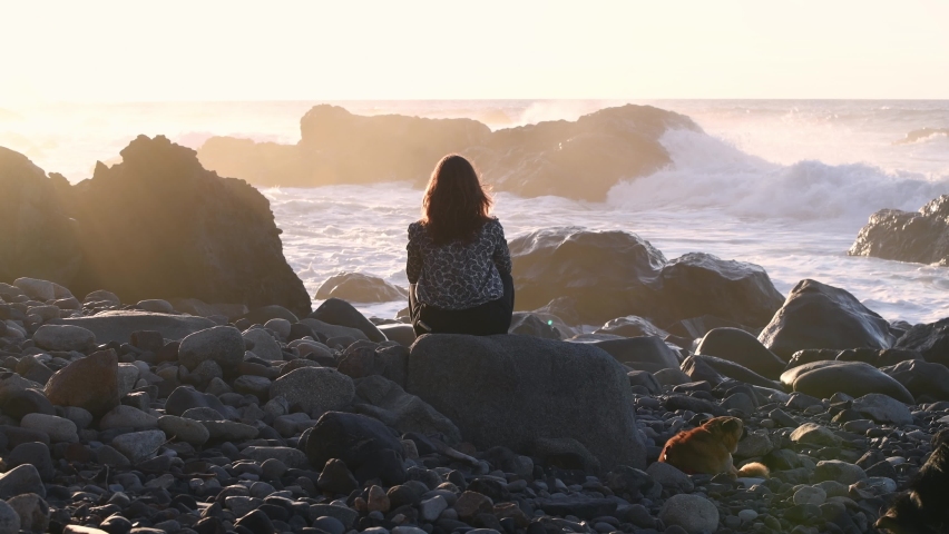Backlit silhouette of a woman from behind watching the sunset in front of the sea at golden hour