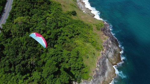 Phuket, Thailand, 25, March, 2022:
Top view of a paraglide dome flying over a tropical coast, drone view of a paraglide flying low above the trees