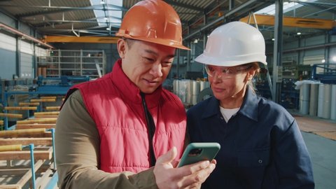 In factory asian man and woman technicians with helmet use mobile phone standing. Engineers, team