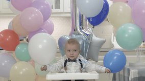 Happy baby boy playing with helium balloons at his first birthday party, one-year-old child against the background of colorful balloons. High quality 4k footage