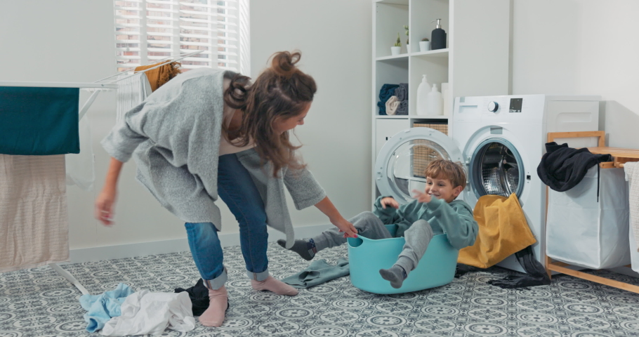 Mom is playing with son who is sitting in laundry bowl little boy wants to spend time with woman and help with household chores mother drags man around laundry room for fun in bowl | Shutterstock HD Video #1088967575