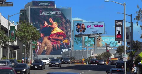 LOS ANGELES, CALIFORNIA, USA - MARCH 19, 2022: Luxury cars traffic on Sunset Strip on Sunset Boulevard at rush hour near giant movie billboard in Los Angeles, California, 4K