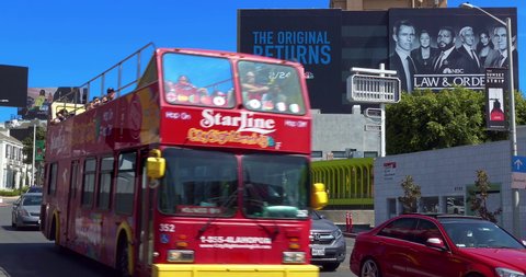 LOS ANGELES, CALIFORNIA, USA - MARCH 19, 2022: Sightseeing tourist bus driving on Sunset Strip on Sunset Boulevard near movie billboard in Los Angeles, California, 4K