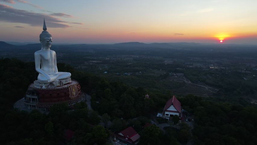 Big white Buddha statue at Wat Phu Manorom on the mountain in Mukdahan Thailand. Image of white Buddha during sunset. Aerial view dolly out. Royalty-Free Stock Footage #1088970151
