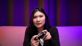 Gamer winning victory moment. Young asian pretty woman sitting on sofa holding joystick in living room. Happy female Professional Streamer chinese playing game online in dark room neon light.