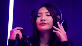 Gamer with controller winning victory moment. Young asian pretty woman sitting on chair with computer pc. Female Professional Streamer wearing headphone playing game online in dark room neon light. - Powered by Shutterstock - Get 15% off with code: PIKWIZARD15