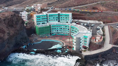 4K drone aerial shot of Los Roques village and damaged hotel building by Atlantic Ocean waves in south Tenerife, Canary Islands