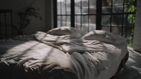 Bed with the white blanket and pillows. Good morning and wake up. Cozy mood, weekend  and relax at home. Gets up from the bed. Greets new day. Sunshine in the window. Modern loft interior.