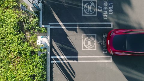 Vertical view on red electric vehicle backing up to park at the EV charging only station. Top down aerial view on zero emission modern vehicle parking to recharge battery in urban landscape at sunset