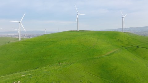 4K aerial of powerful Wind turbine farm for energy production on beautiful cloudy sky at scenic green hills. Wind power turbines generating clean renewable energy for sustainable development footage
