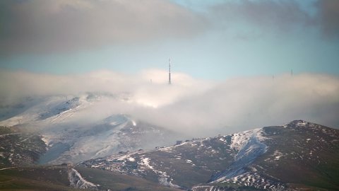 8K 7680x4320. Cloud flowing down the ridge of the mountain range.Mist lying in the folds of hills.Treeless lands.Snowy hills summit peak in nature. Fog disappears fogs transmitting antenna tower winter.