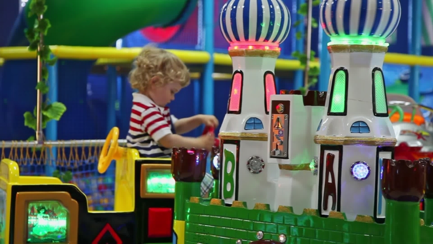 The kid rides on the carousel. The boy is riding a toy train. A colorful locomotive moves along the rails around the caramel towers.