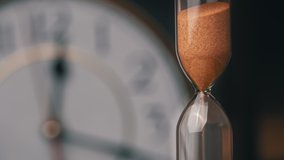 Hourglass close-up is pouring against the background ordinary mechanical watch. The sand is pouring and counting the time. Time flows, the transience of time. Countdown, minutes, seconds, hours. - Powered by Shutterstock - Get 15% off with code: PIKWIZARD15