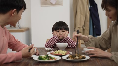 slow motion of picky Asian boy shaking head while refusing food his father and mother put in his bowl during lunch time in dining room at home