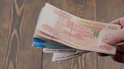 caucasian hand shaking small stack of russian ruble banknotes over blurry wooden background, closeup witth slow motion