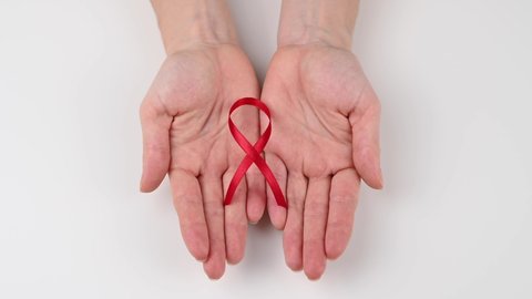 A woman opens her hands and shows a red ribbon on a white background. Symbol of the fight against AIDS.